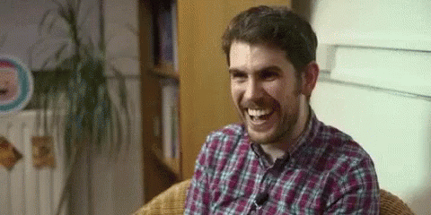 A Man In A Plaid Shirt Is Sitting In A Chair And Laughing . GIF
