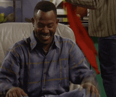 A Man In A Plaid Shirt Is Sitting In A Chair And Laughing GIF