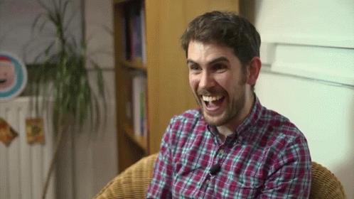 A Man In A Plaid Shirt Is Sitting In A Chair And Smiling GIF