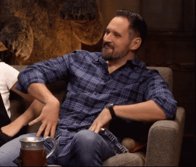 A Man In A Plaid Shirt Is Sitting In A Chair With His Hands On His Knees . GIF
