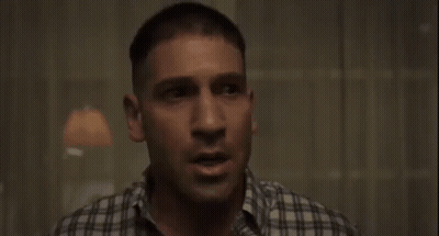 A Man In A Plaid Shirt Is Sitting In A Dark Room GIF
