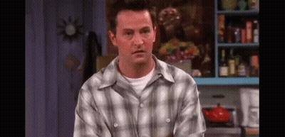 A Man In A Plaid Shirt Is Sitting In A Kitchen Looking At The Camera . GIF