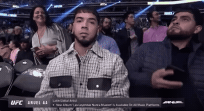 A Man In A Plaid Shirt Is Sitting In A Ufc Stadium GIF