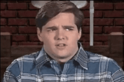 A Man In A Plaid Shirt Is Sitting In Front Of A Brick Wall . GIF