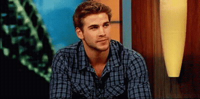A Man In A Plaid Shirt Is Sitting In Front Of A Lamp And Looking At The Camera . GIF
