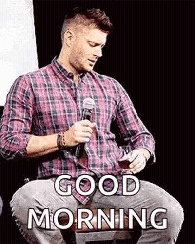 A Man In A Plaid Shirt Is Sitting In Front Of A Microphone And Holding A Glass Of Wine . GIF