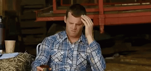 A Man In A Plaid Shirt Is Sitting In Front Of A Pile Of Hay And Holding His Head . GIF