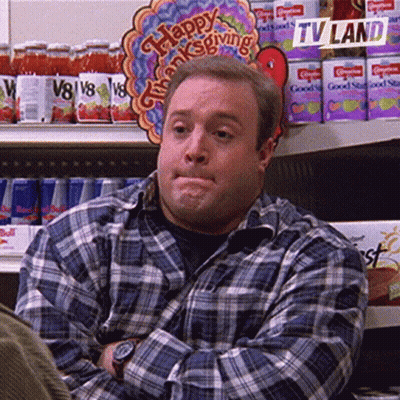 A Man In A Plaid Shirt Is Sitting In Front Of A Sign That Says Happy Thanksgiving On It . GIF