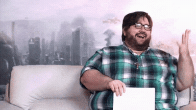 A Man In A Plaid Shirt Is Sitting On A Couch And Holding A Piece Of Paper GIF