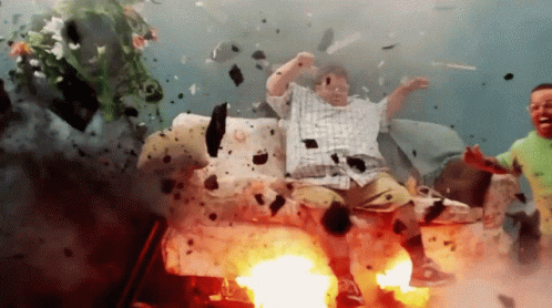 A Man In A Plaid Shirt Is Sitting On A Couch In An Explosion GIF