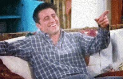 A Man In A Plaid Shirt Is Sitting On A Couch Pointing GIF