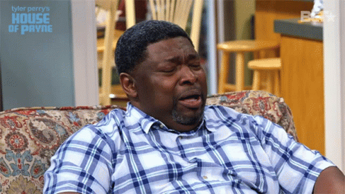 A Man In A Plaid Shirt Is Sitting On A Couch With The Words Tyler Perry 'S House Of Payne GIF