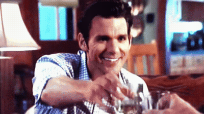 A Man In A Plaid Shirt Is Smiling While Holding A Glass Of Water GIF