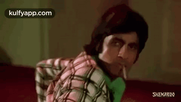 A Man In A Plaid Shirt Is Smoking A Cigarette While Sitting On A Red Couch . GIF