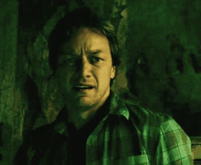 A Man In A Plaid Shirt Is Standing In A Dark Room GIF