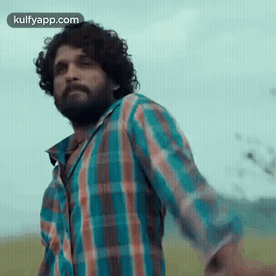 A Man In A Plaid Shirt Is Standing In A Field With His Arms Outstretched . GIF