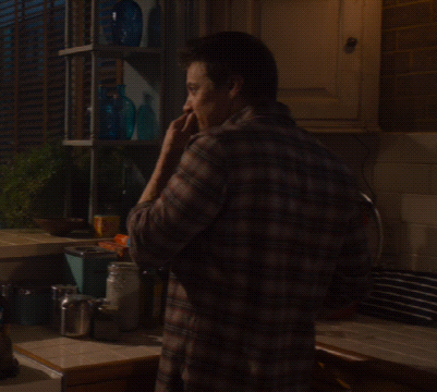 A Man In A Plaid Shirt Is Standing In A Kitchen Talking On A Cell Phone GIF