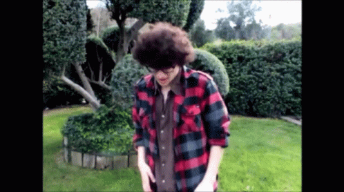 A Man In A Plaid Shirt Is Standing In A Yard GIF