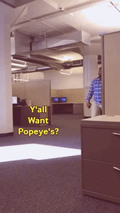 A Man In A Plaid Shirt Is Standing In An Office With The Words " Y'all Want Popeye 'S " GIF
