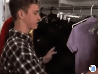 A Man In A Plaid Shirt Is Standing In Front Of A Closet Full Of Clothes . GIF