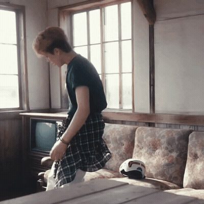 A Man In A Plaid Shirt Is Standing In Front Of A Couch GIF