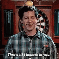 A Man In A Plaid Shirt Is Standing In Front Of A Dart Board . GIF
