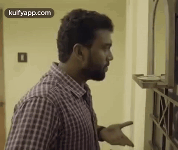 A Man In A Plaid Shirt Is Standing In Front Of A Mirror And Talking To Someone . GIF