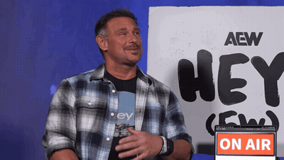 A Man In A Plaid Shirt Is Standing In Front Of A Sign That Says Hey GIF