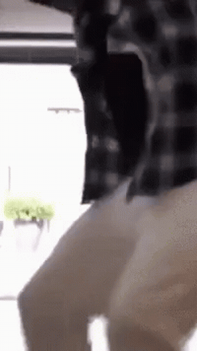 A Man In A Plaid Shirt Is Standing In Front Of A Window And Dancing . GIF