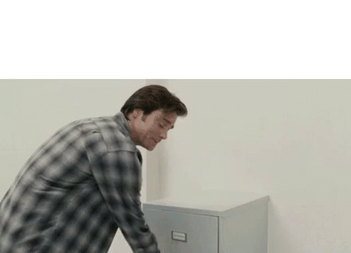 A Man In A Plaid Shirt Is Standing Next To A Filing Cabinet . GIF