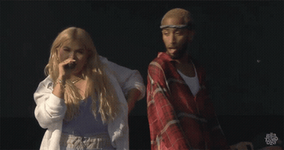 A Man In A Plaid Shirt Is Standing Next To A Woman In A White Shirt That Says Hayley Bravo On The Bottom GIF