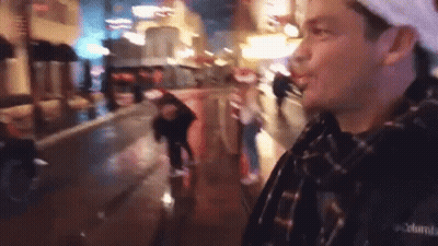 A Man In A Plaid Shirt Is Standing On A Wet City Street At Night . GIF