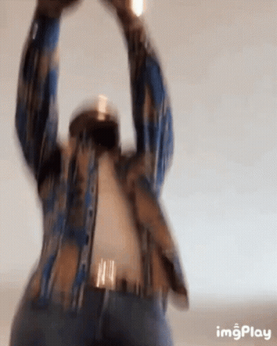 A Man In A Plaid Shirt Is Standing With His Arms In The Air . GIF