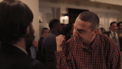 A Man In A Plaid Shirt Is Talking To Another Man In A Crowd GIF