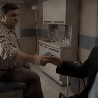A Man In A Plaid Shirt Is Talking To Another Man In A Kitchen GIF