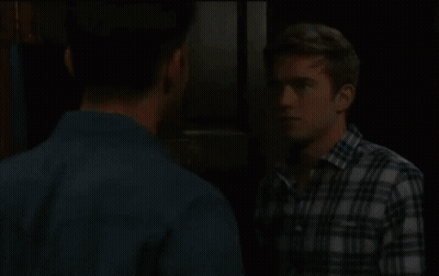 A Man In A Plaid Shirt Is Talking To Another Man GIF