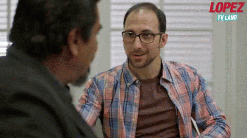 A Man In A Plaid Shirt Is Talking To Another Man With The Words Lopez Tv Land Behind Him GIF
