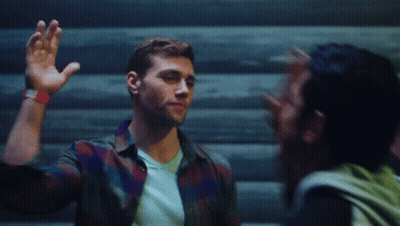 A Man In A Plaid Shirt Is Waving His Hand At Another Man GIF