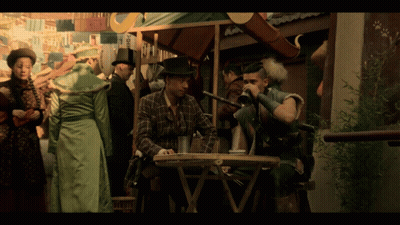 A Man In A Plaid Shirt Sits At A Table Drinking From A Glass GIF