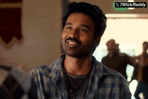A Man In A Plaid Shirt Smiles In Front Of A Sign That Says X7wickreddy GIF