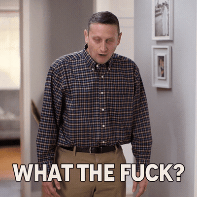 A Man In A Plaid Shirt Stands In A Hallway And Says " What The Fuck " GIF