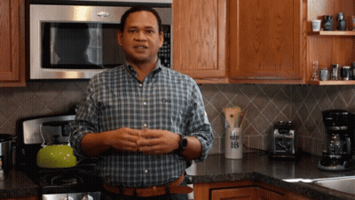 A Man In A Plaid Shirt Stands In A Kitchen In Front Of A Microwave And A Container With The Letter B On It GIF