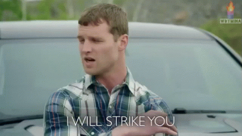 A Man In A Plaid Shirt Stands In Front Of A Car And Says I Will Strike You GIF