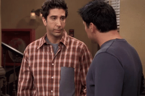A Man In A Plaid Shirt Stands Next To Another Man In A Blue Shirt GIF