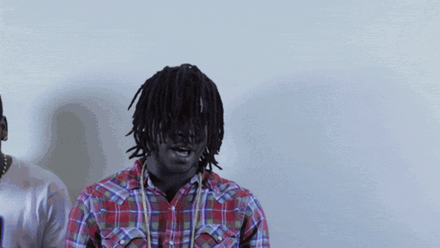 A Man In A Plaid Shirt Stands Next To Another Man In A White Shirt GIF