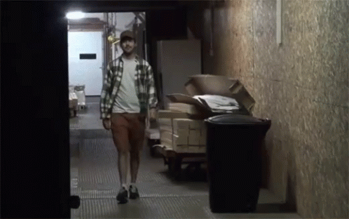 A Man In A Plaid Shirt Walks Down A Hallway GIF