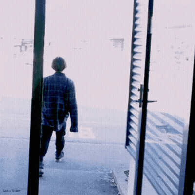 A Man In A Plaid Shirt Walks Down The Street GIF