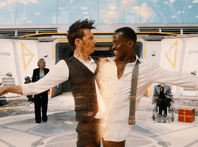 A Man In A Plaid Vest Is Holding A Man In A White Shirt GIF