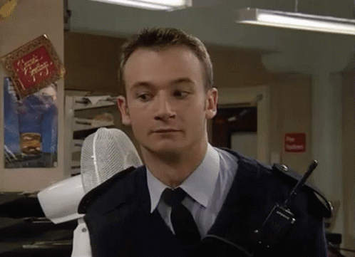A Man In A Police Uniform And Tie Is Holding A Walkie Talkie In A Room . GIF