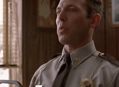 A Man In A Police Uniform And Tie Is Sitting In A Room Talking To Someone . GIF
